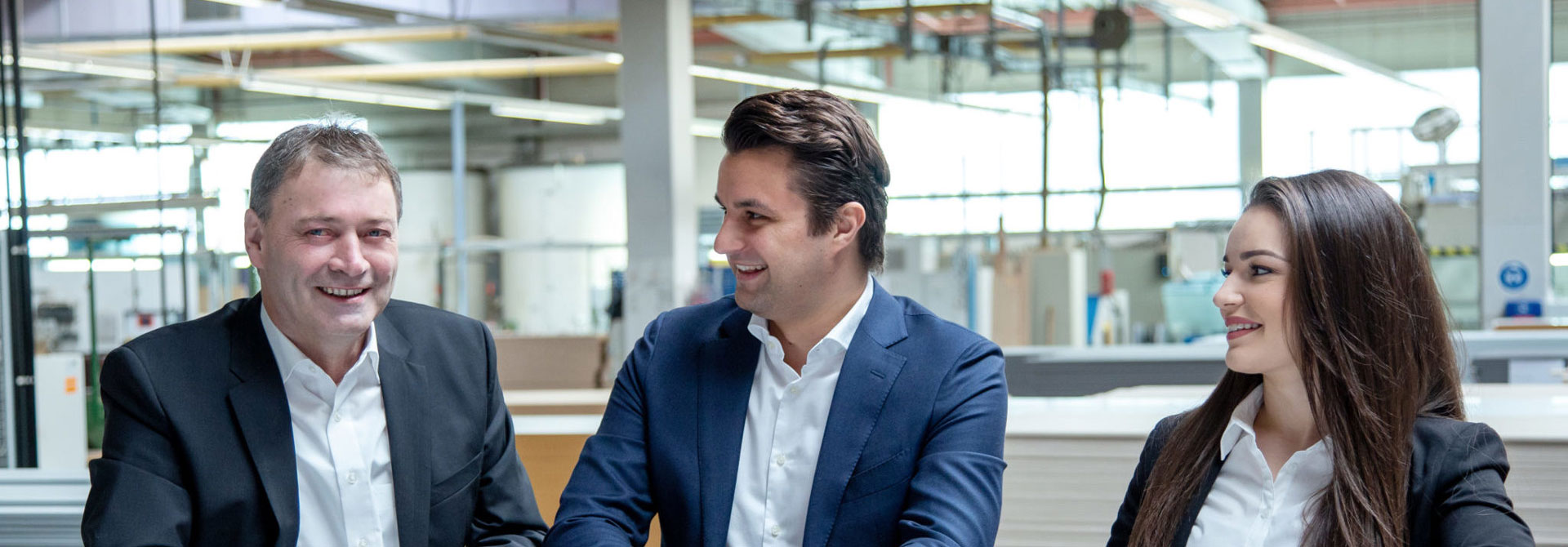 Trois personnes en costume sourient au bureau.